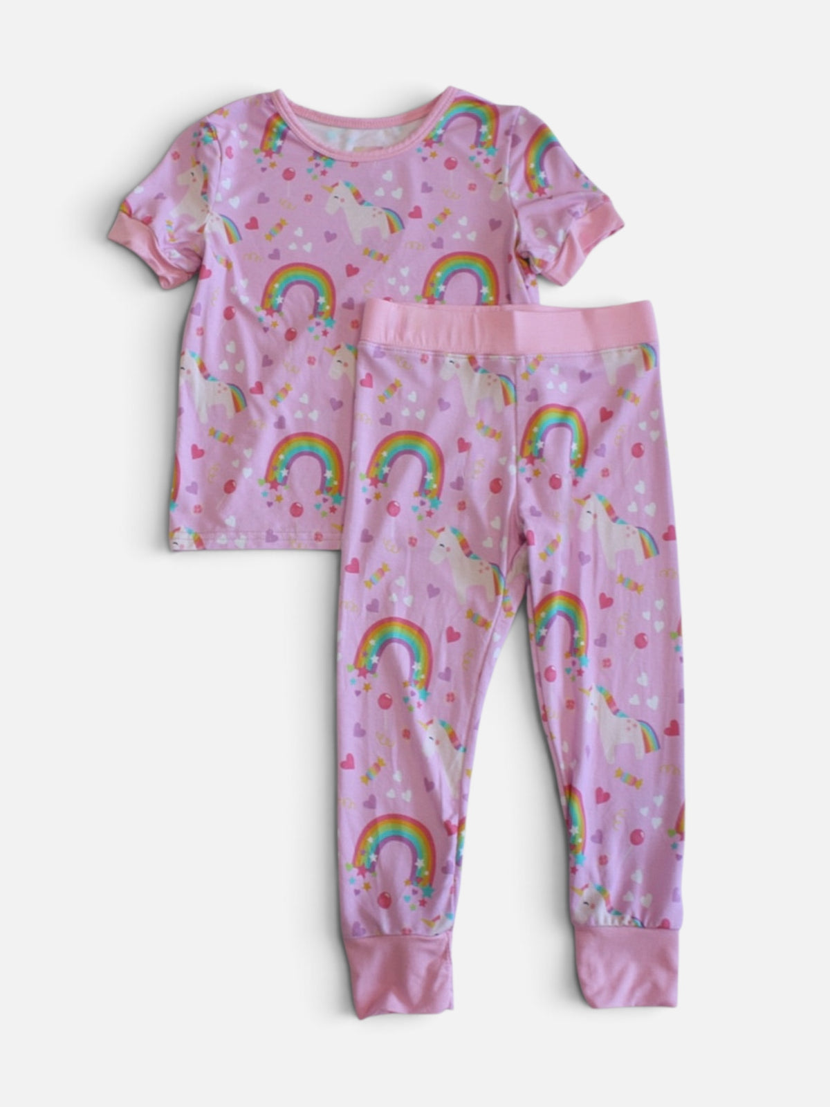 A two-piece children's bamboo viscose pajama set featuring a short-sleeve top and matching  pants in pink, both printed with colorful rainbows, unicorns, and small hearts.