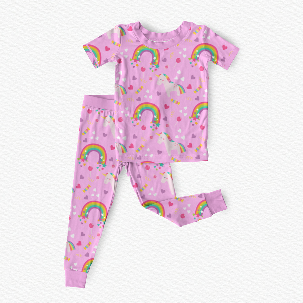 Polly & Pearl two-piece children's bamboo viscose  pajama set in l pink, featuring a short-sleeve top and matching pants with an all-over print of rainbows, unicorns, hearts, and stars.