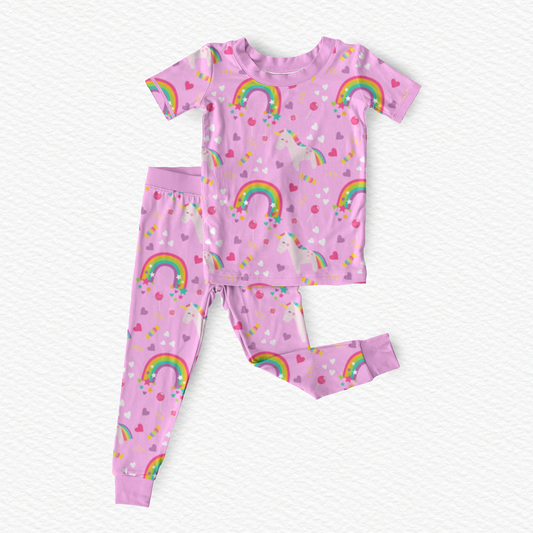 Polly & Pearl two-piece children's bamboo viscose  pajama set in l pink, featuring a short-sleeve top and matching pants with an all-over print of rainbows, unicorns, hearts, and stars.