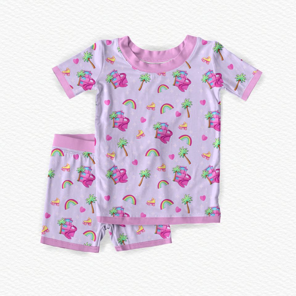 A two-piece children's bamboo viscose pajama set featuring a short-sleeve top and matching shorts in light lavender  decorated with a colorful tropical and beach-themed print including palm trees, rainbows, and hearts, yellow roller skates, palm tress, and a doll  dreamhouse 